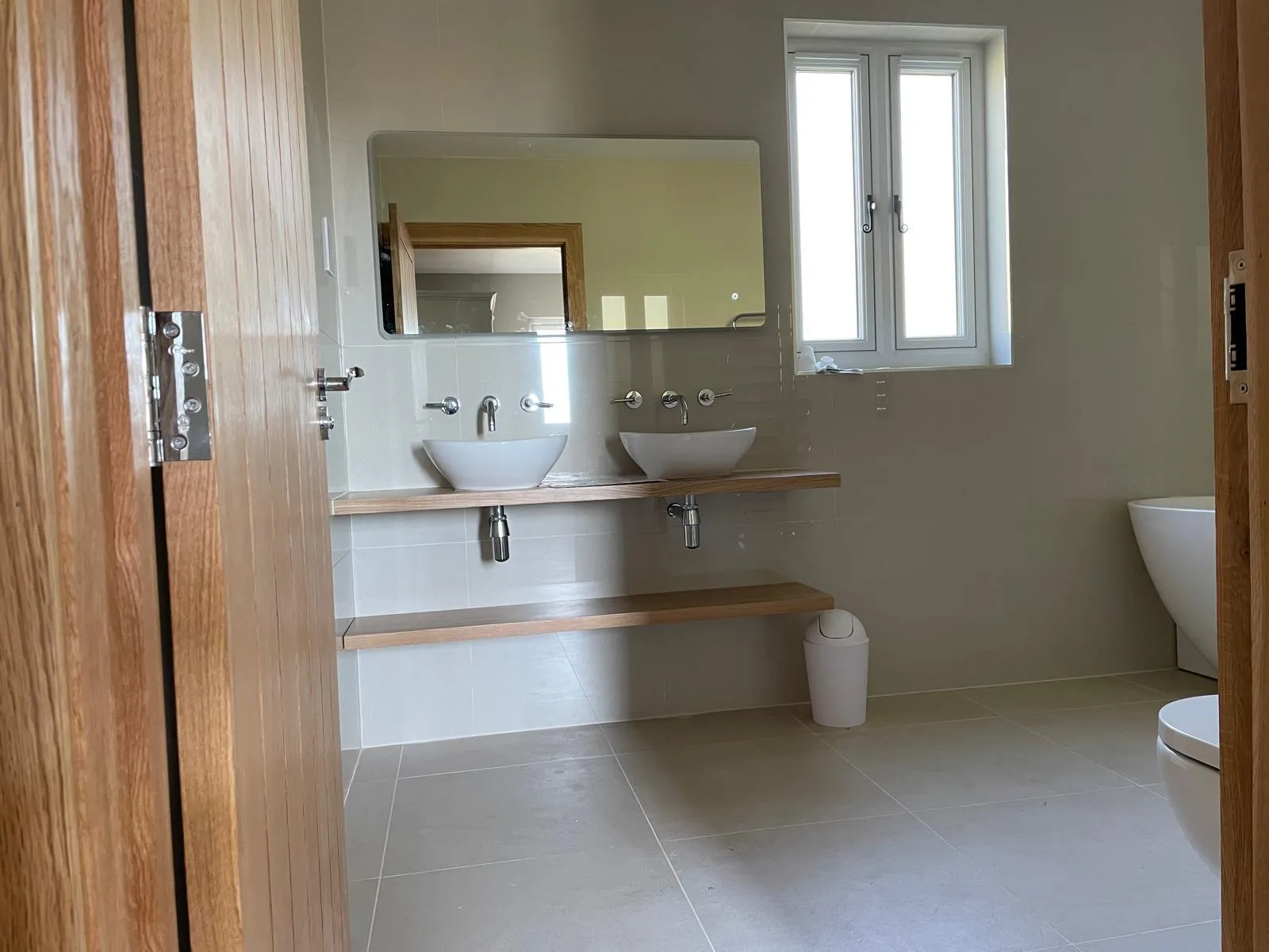 Two vessel basins on an oak shelf in a bathroom with large tiles