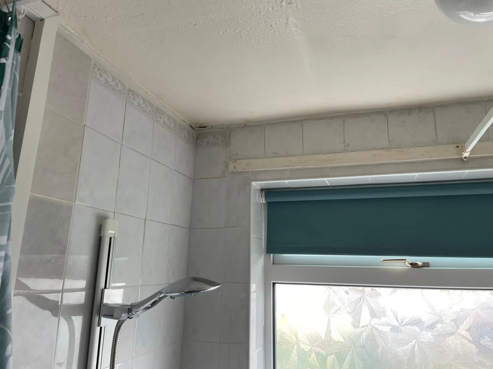 Old bathroom with dated white tiles, a shower rail and a teal blind, before the work