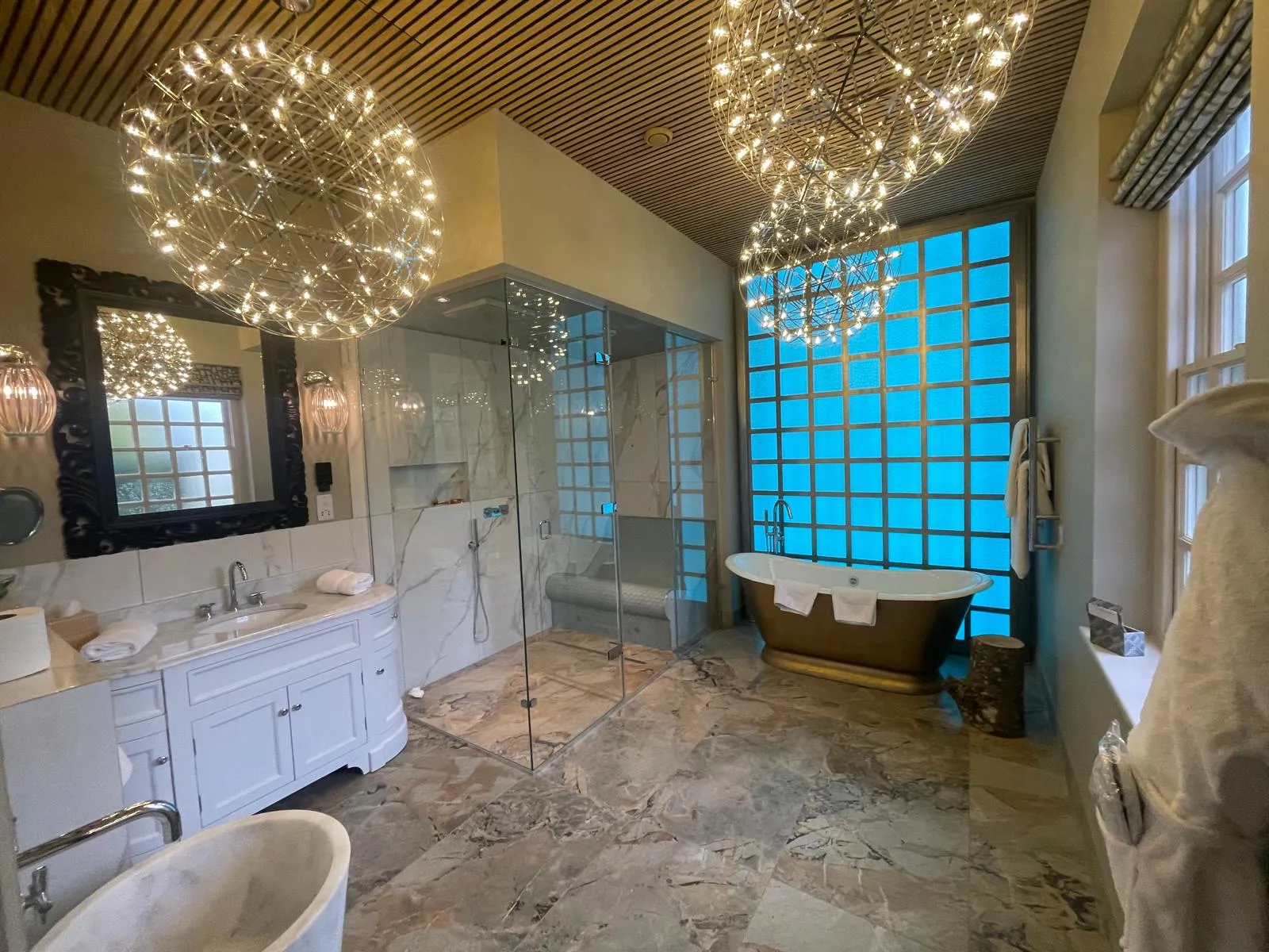 Marble bathroom with a glass shower enclosure and a bronze freestanding bath